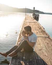 a man and a child sitting on a dock with swans in the background