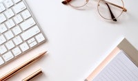 a white desk with a keyboard, glasses and a pen