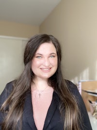 a woman in a black blazer and pink shirt smiling